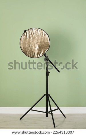Studio reflector on tripod near pale green wall indoors. Professional photographer's equipment
