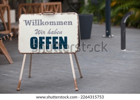 Outdoor open sign with written in it in German: "Willkommen wir haben offen.", meaning in English "Bienvenue nous sommes ouverts.".
