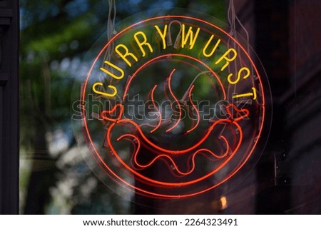 Circular neon light at a restaurant's window showing a Curry wurst.