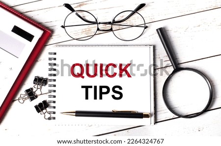 Office desk with calculator, notebook with QUICK TIPS text, magnifying glass, paper clips, glasses and pen. View from above