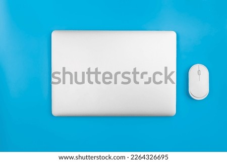 Closed laptop and computer mouse on a blue background, top view. Royalty-Free Stock Photo #2264326695