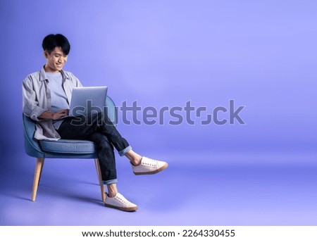 full body image of young asian man using laptop on purple background
