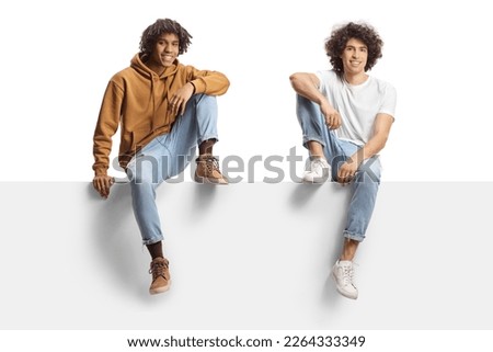 African american young man and a caucasian young man sitting on a blank panel isolated on white background