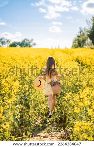 girl runs into a field of rapeseed. Yellow flower field. View from the back