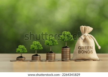 The tree grows on a pile of coins and a money bag in the word green Bonds with green background. Investment on bonds concept. Raising funds to fund environmentally friendly projects.Green bonds. Royalty-Free Stock Photo #2264341829
