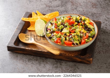 Cowboy caviar or Texas salad is made with beans, corn, bell peppers, and tomato in chili lime vinaigrette for a delicious party appetizer closeup in the bowl on the wooden board. Horizontal
