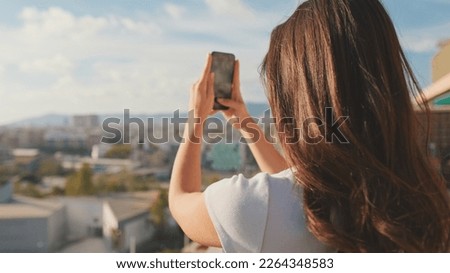 Close up, young woman takes photo on mobile phone while standing on the balcony at home.