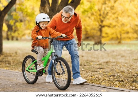 Happy family grandfather teaches boy grandson  to ride a bike in autumn park   in nature