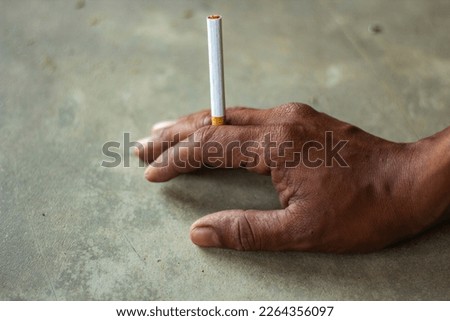 This is a man holding a cigarette in his hand and the background behind him is blurred