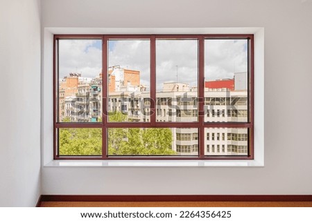 Large window in the room with a wide window sill. Window in plastic brown frame. Through the window you can watch what is happening on the street and the neighboring houses opposite. Royalty-Free Stock Photo #2264356425