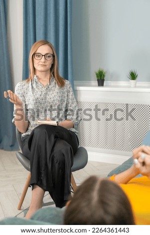 Female psychologist talks and helps the girl. Record important research on a tablet, rear view. Psychology, concept of mental health of people. Vertical photo. Appointment with a psychotherapist.