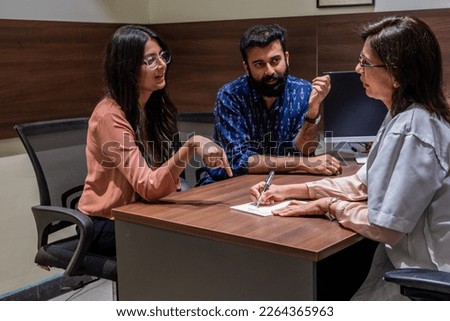 An urban Indian couple consult a female health care practitioner in her clinic, while seated indoors in a modern office in New Delhi, patiently listening to the medical professional's reports. Royalty-Free Stock Photo #2264365963