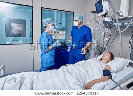 Female unconscious patient attached to medical monitoring equipment in intensive care unit with hospital nurses. ICU Royalty-Free Stock Photo #2264370117