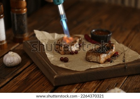 Cooking meat medallions with manual gas burner on wooden table in photo studio. Food stylist