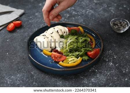 Food stylist preparing delicious salad with mozzarella and tomatoes for photoshoot at dark grey table in studio, closeup