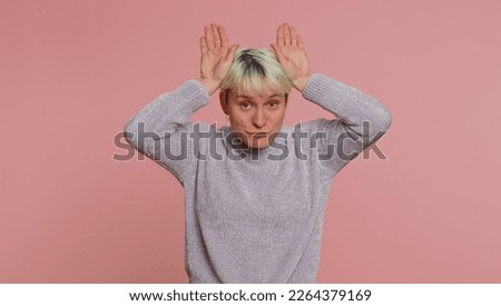 I am little bunny rabbit. Lovely funny woman with short hair smiling friendly and doing bunny ears gesture on head, having fun, fooling with humorous comical mood. Young adult girl on pink background
