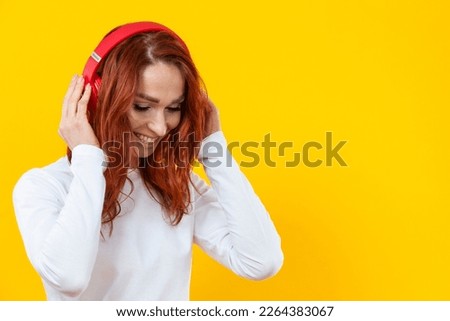 Smiling happy friendly woman in white casual shirt t-shirt wearing red wireless headphones isolated on yellow background studio portrait.Horizontal Shot