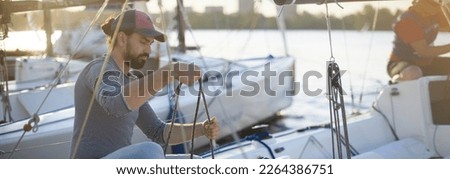 Preparation for the regatta at the yachting school at the marina with sailing yachts. Students and coaches prepare moored sports yachts for sailing on a sunny summer day. Royalty-Free Stock Photo #2264386751