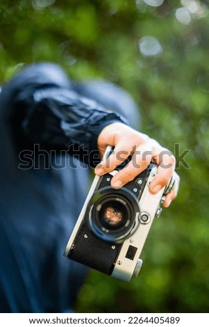 film camera in the hands of a girl taking a picture. Green trees bokeh background, woman taking a photo with camera