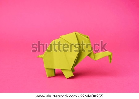 Yellow paper elephant on pink background. Origami art