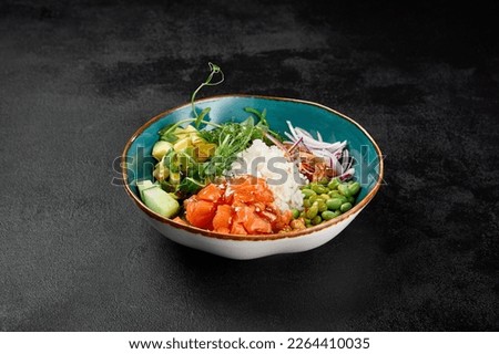 Poke bowl with salmon and vegetables on black concrete background. Ahi poke with salmon, rice, edamame and sauce. Poke bowl in minimal style on black background. Salad bowl with salmon