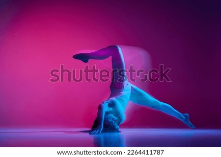 Dynamic portrait of young flexible woman dancing contemp, freestyle dance on gradient pink studio background in neon with mixed lights. Concept of contemporary dance style, art, aesthetics, creativity Royalty-Free Stock Photo #2264411787