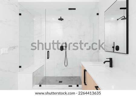 A beautiful luxury, modern bathroom with a light wood cabinet, walk-in shower with marble tiled walls, and black faucets and hardware. Royalty-Free Stock Photo #2264413635