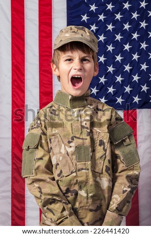 Young boy dressed like a soldier with American flag in background.