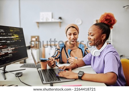 Side view portrait of two young women working on software development project together and smiling happily Royalty-Free Stock Photo #2264418721