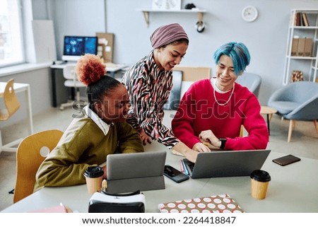Diverse group of creative young people using laptop during meeting in office and smiling cheerfully Royalty-Free Stock Photo #2264418847