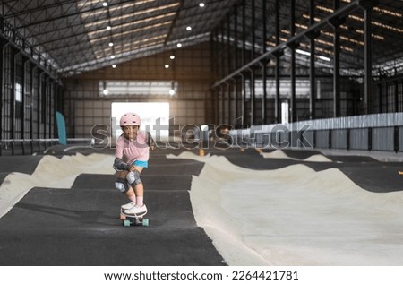 asian child skater or kid girl fun playing skateboard or smile ride surf skate in indoor pump track in skate park by extreme sports surfing to wear helmet elbow pads wrist knee guard for body safety Royalty-Free Stock Photo #2264421781