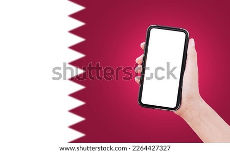 Close-up of male hand holding smartphone with blank on screen, on background of blurred flag of Qatar.