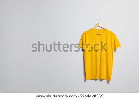 Hanger with yellow t-shirt on light wall. Mockup for design