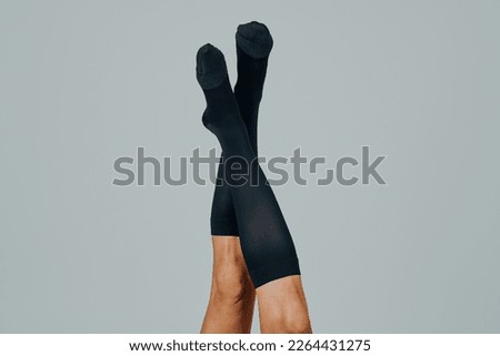 the legs of a man, upside down, wearing compression socks, in front of an off-white background with some blank space around him