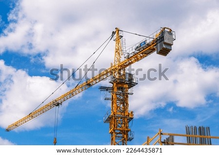 A tower construction crane on the background of a blue sky with clouds. Boom rotary crane with boom. Construction of apartment buildings in the city.