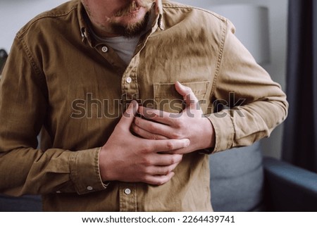 Male having cardiac medical health problem painful sickness symptoms myocardial infarction. Close up of young man pressing hand chest heart attack suffering from unbearable pain sit on sofa at home Royalty-Free Stock Photo #2264439741