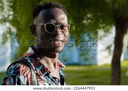 keep your spirits up with a good smile, young african man with glasses, looking at the camera standing outdoors at sunset.