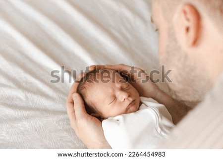 Close up of caucasian hairy brunet cute newborn baby sleeping.One or two week child on bed in male hands.Unrecognizable man, father,holding child.Care,love,happiness concept.