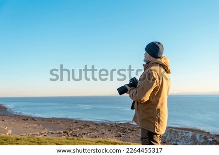 Bearded Man reaching the destination  at sunset on cool day and taking photos of amazing seaside landscape in Wales. Travel Lifestyle concept.