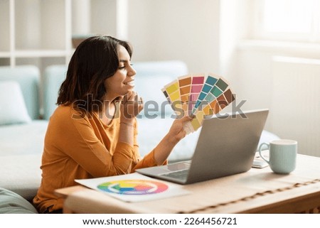 Middle Eastern Female Freelancer Holding Color Swatches And Using Laptop At Home, Arab Graphic Designer Woman Choosing Colour Palette For New Project And Working Online On Computer, Free Space