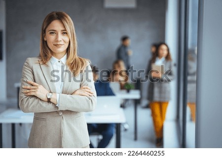 Portrait of young smiling woman looking at camera with crossed arms. Happy girl standing in creative office. Successful businesswoman standing in office with copy space. Urban happy business woman