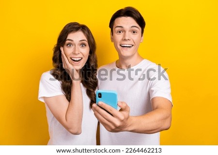 Photo of adorable impressed husband wife dressed t-shirts getting messages modern gadget isolated yellow color background