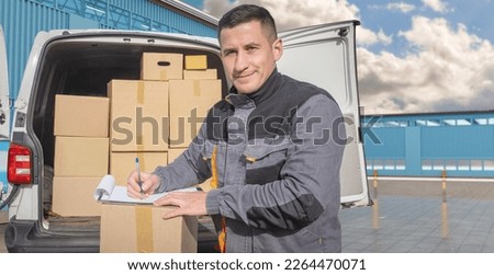 Man courier near minivan. Guy works for courier company. Delivery man smiles as he signs paper. Courier with clipboard near warehouse building. Transport company employee. 