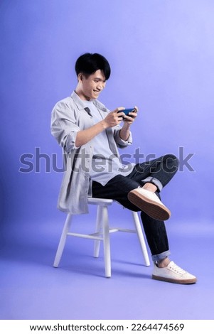full body image of young asian man using phone on purple background
