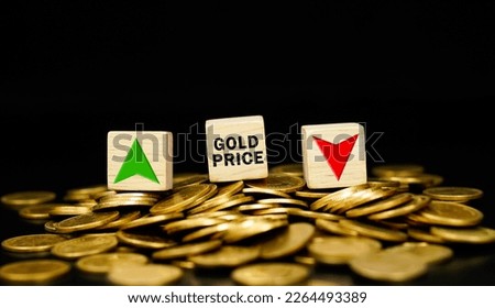 Wooden cubes with the word gold price and arrows pointing up and down on stacks of gold coins. Changing gold price trend goes down or up. Gold price level.	                         