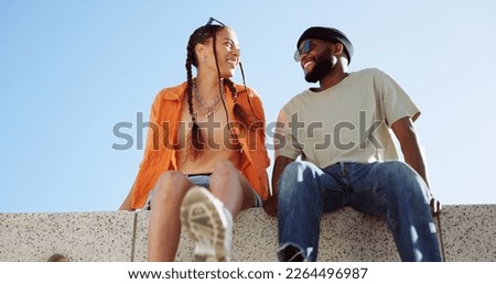 Couple, city and relax with a black man and woman sitting on a wall outdoor against a clear blue sky together. Street style, travel and love with a happy male and female bonding outside during summer Royalty-Free Stock Photo #2264496987