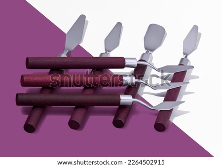 Seven palette knives on a white-purple background with a hard light. Close-up.