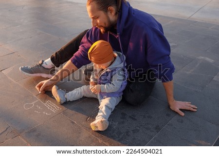 Dad and child draw with chalk on the pavement. Autumn day.