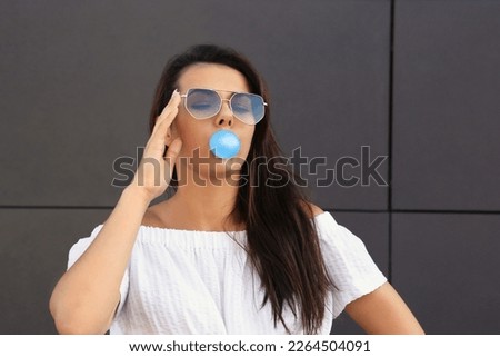 Beautiful woman blowing gum near dark tiled wall