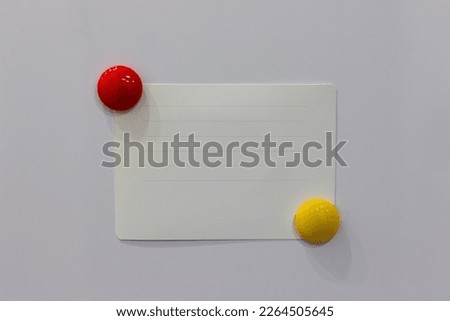 A clean white sheet of paper is attached to the refrigerator with a round, bright magnet. For notes, lists, a blank white sheet on a white refrigerator.